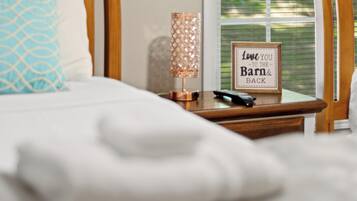 A neatly made bed with a white comforter and a blue patterned pillow. A bedside table with a lamp and a framed sign saying 'Love you to the barn & back' is visible.