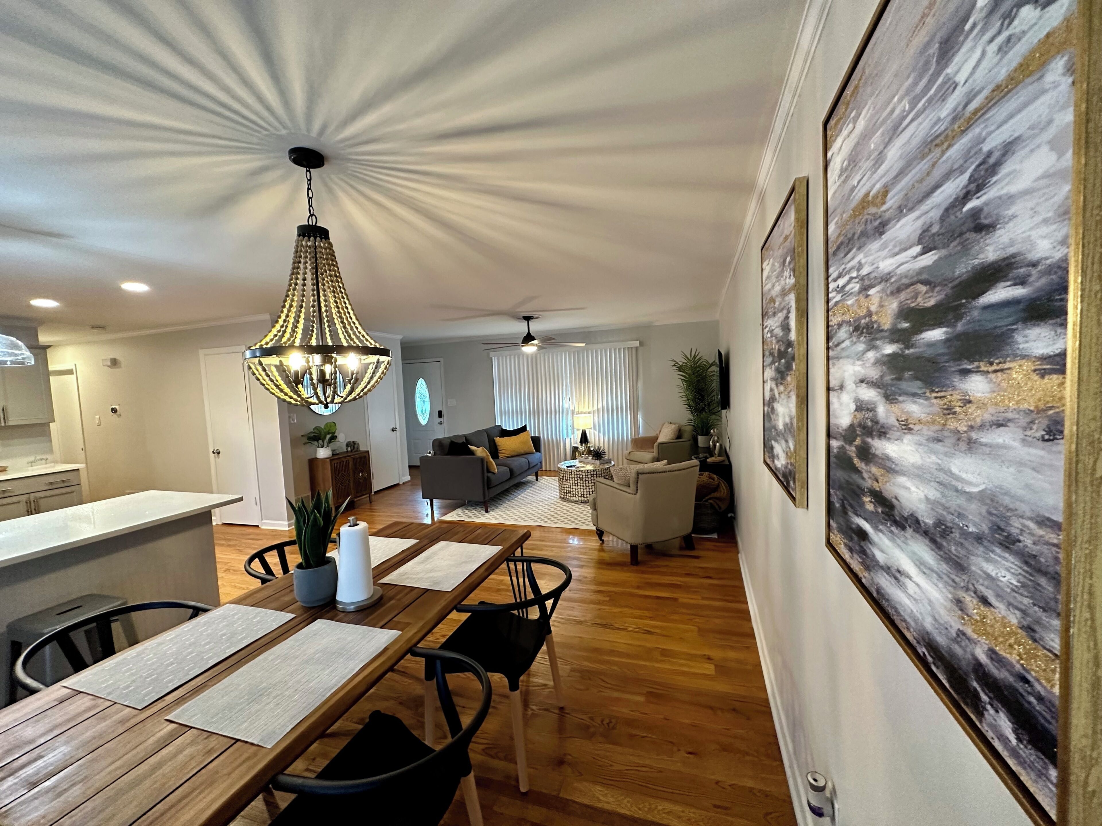 A spacious living area with a dining table, chairs, a chandelier, and a large abstract painting on the wall.