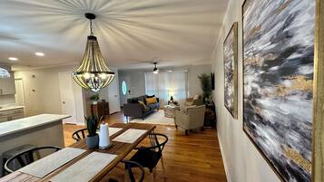 A spacious living area with a dining table, chairs, a chandelier, and a large abstract painting on the wall.