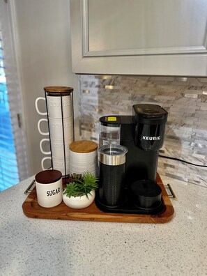 A kitchen counter with a coffee maker, sugar container, and stacked coffee mugs.