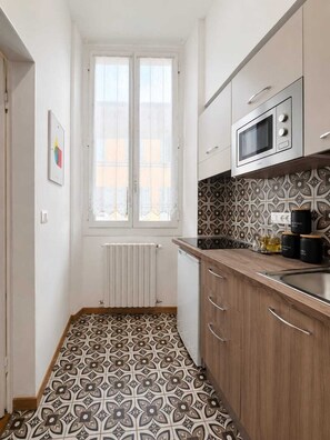 A kitchen with a window, white cabinets, a microwave, and patterned floor tiles. - Il Salotto Suite (Bologna)