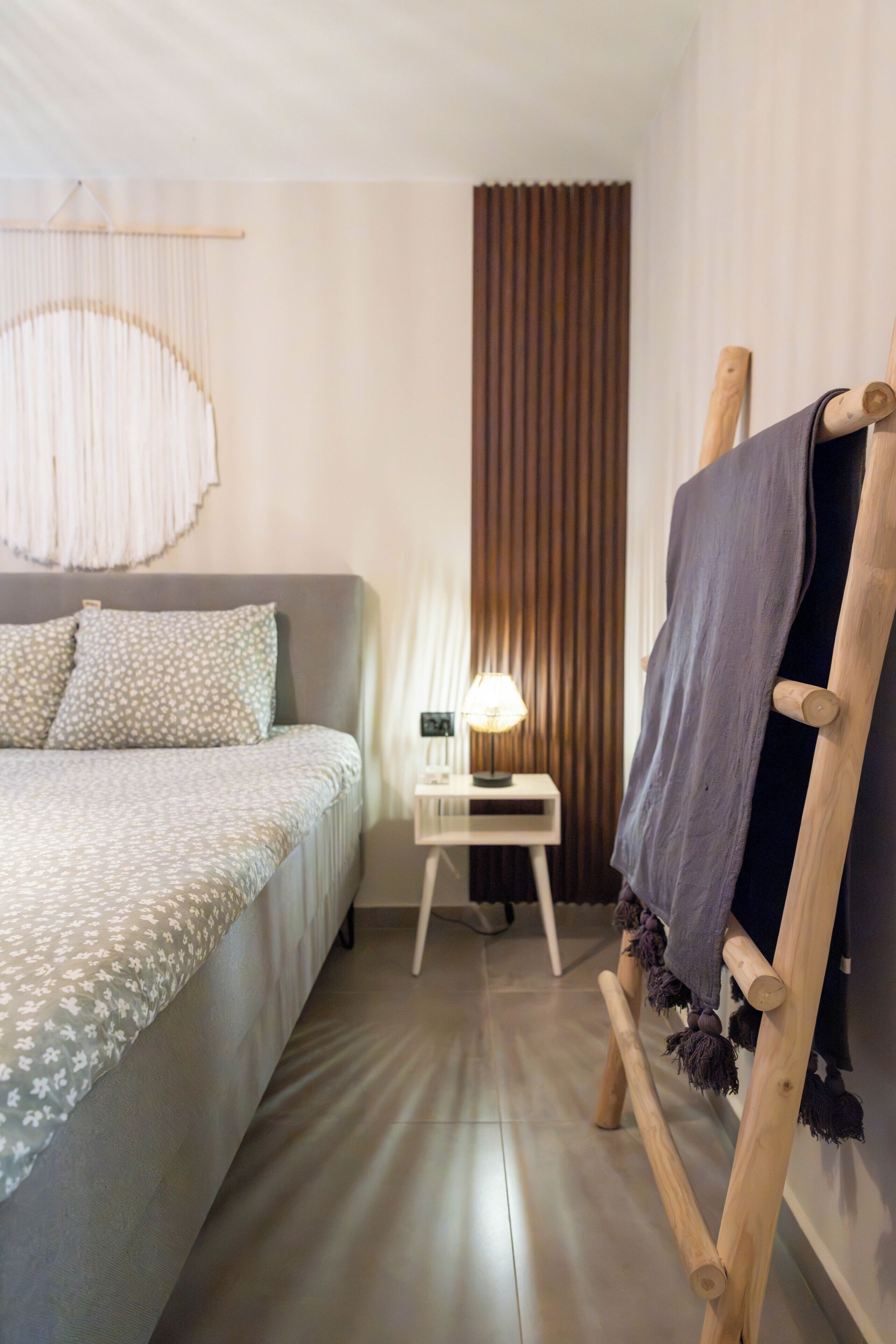 A hotel room with a bed, a nightstand, a lamp, a curtain, and a wooden chair.