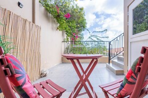 Ein Balkon mit Tisch und zwei Stühlen, einem Bambuszaun und Blick auf einen Garten mit rosa Blumen.