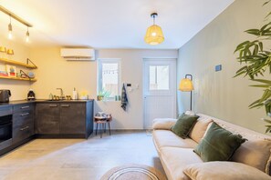 Eine moderne Küche mit Backofen, ein Essbereich mit Sofa und Couchtisch sowie ein großes Fenster, das natürliches Licht hereinlässt.