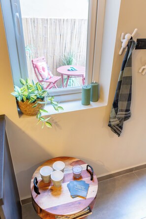 Ein Zimmer mit Fenster, ein kleiner Tisch mit Tassen und einer Kerze, eine Pflanze sowie ein Handtuchhalter an der Wand.