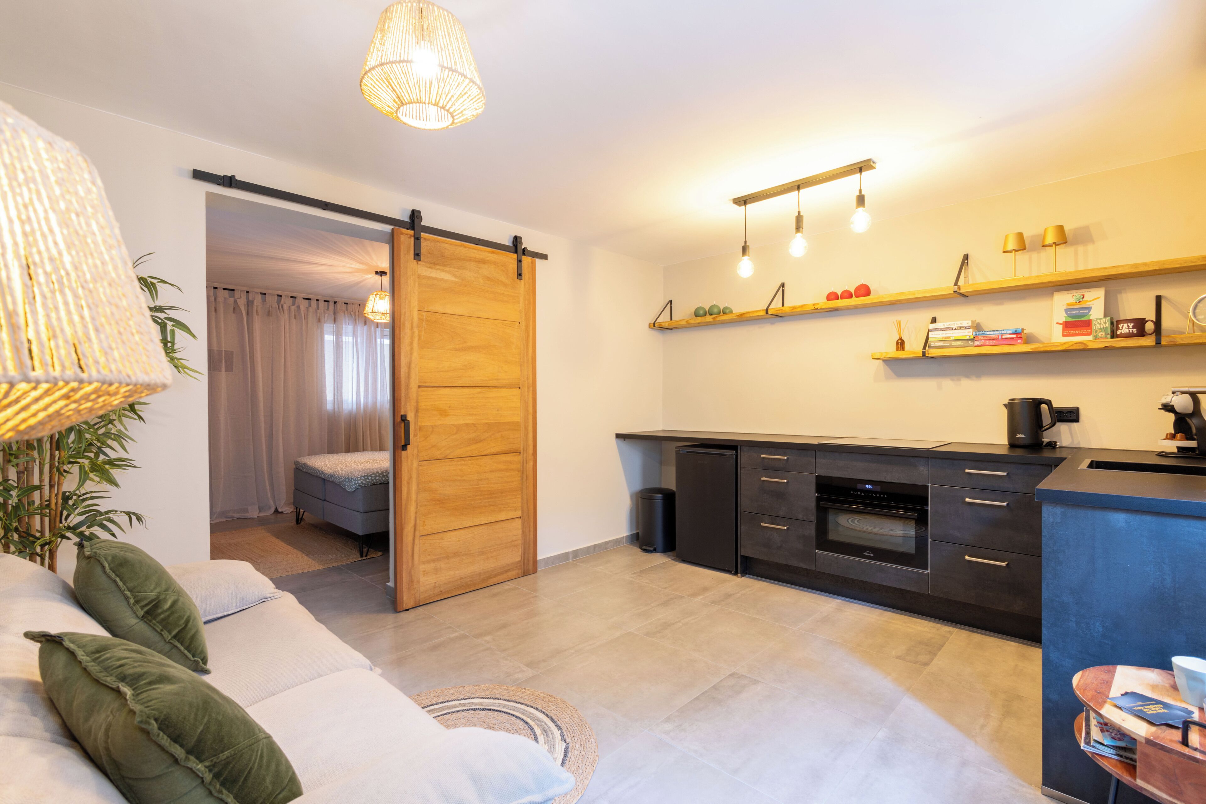 Een moderne keuken met een schuifdeur naar een slaapkamer, een eethoek, en een woonkamer met een bank en een lamp.