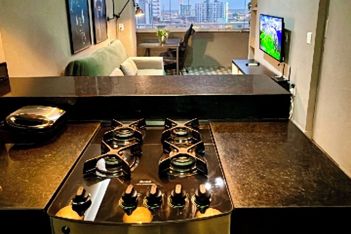 A modern kitchen with a gas stove, pendant lights, and a view of the cityscape.