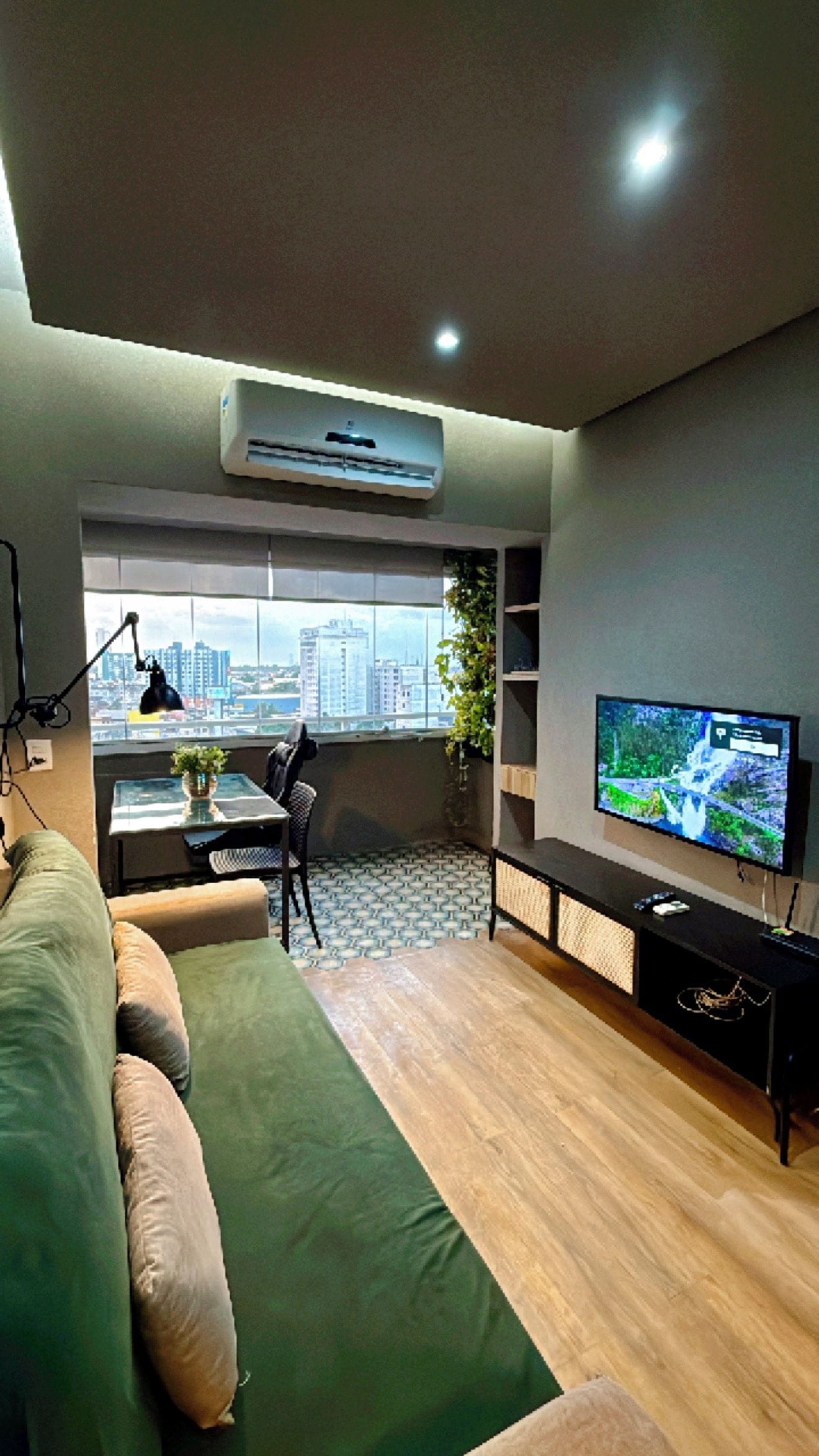 A modern living room with a sofa, a TV, a desk, and a view of the city.