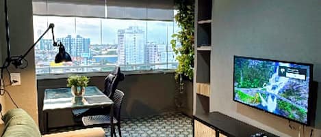 Una sala moderna con sofá, televisor, escritorio y vista a la ciudad.