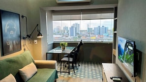 A small living space with a sofa, a dining table with chairs, a TV, and a view of a cityscape through a window. - Loft no Studio Unique com Garagem 1104 (Belem)