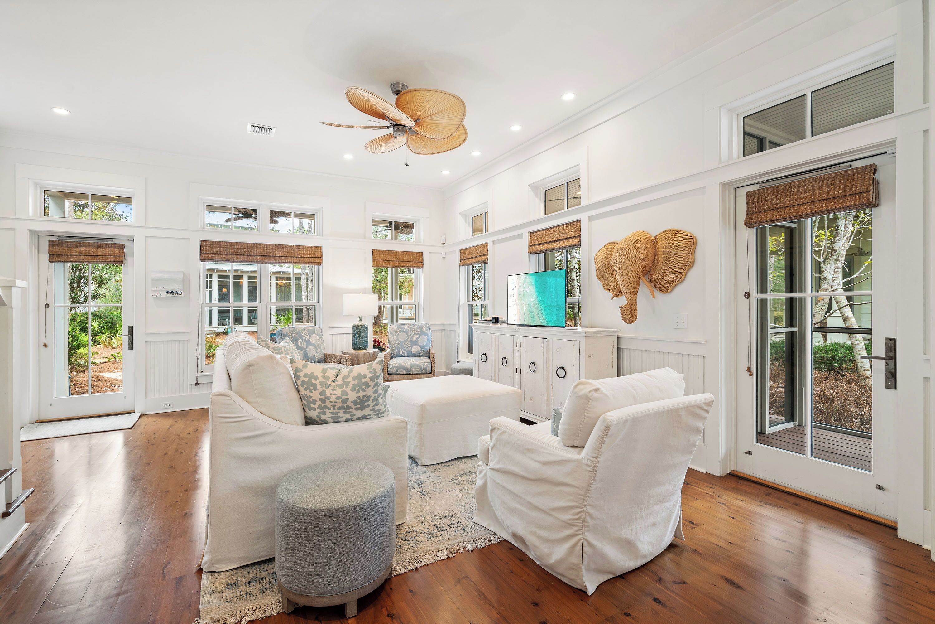 A spacious living area with a ceiling fan, white furniture, and large windows.
