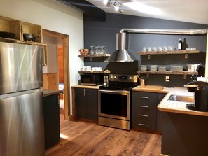 A modern kitchen with stainless steel appliances, wooden flooring, and built-in shelves.