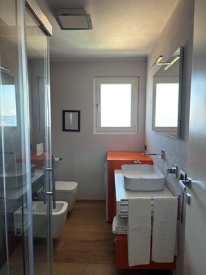 Un bagno moderno con box doccia in vetro, un water bianco, un lavabo con mobile contenitore e una finestra che offre luce naturale.