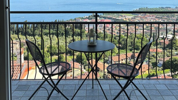 Un balcon avec une table et deux chaises, donnant sur une ville côtière et la mer.