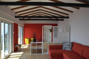 Ein modernes Wohnzimmer mit roter Akzentwand, einem weißen Regalsystem, einem roten Sofa und einem gelben Sessel.