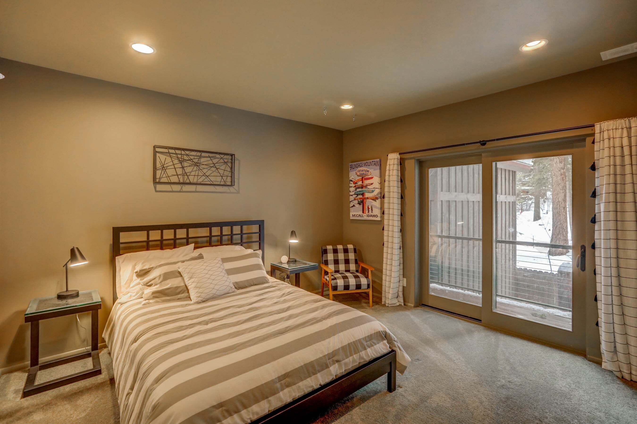 A bedroom with a bed, a nightstand, a chair, a poster, and a sliding glass door leading to a snowy outdoor area.