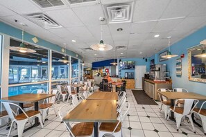 Een restaurant met meerdere tafels en stoelen, een toonbank en een televisiescherm.
