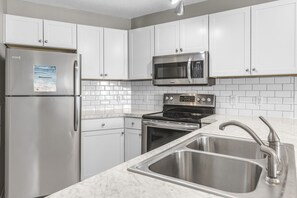 Una cocina moderna con electrodomésticos de acero inoxidable, armarios blancos y encimera de mármol.
