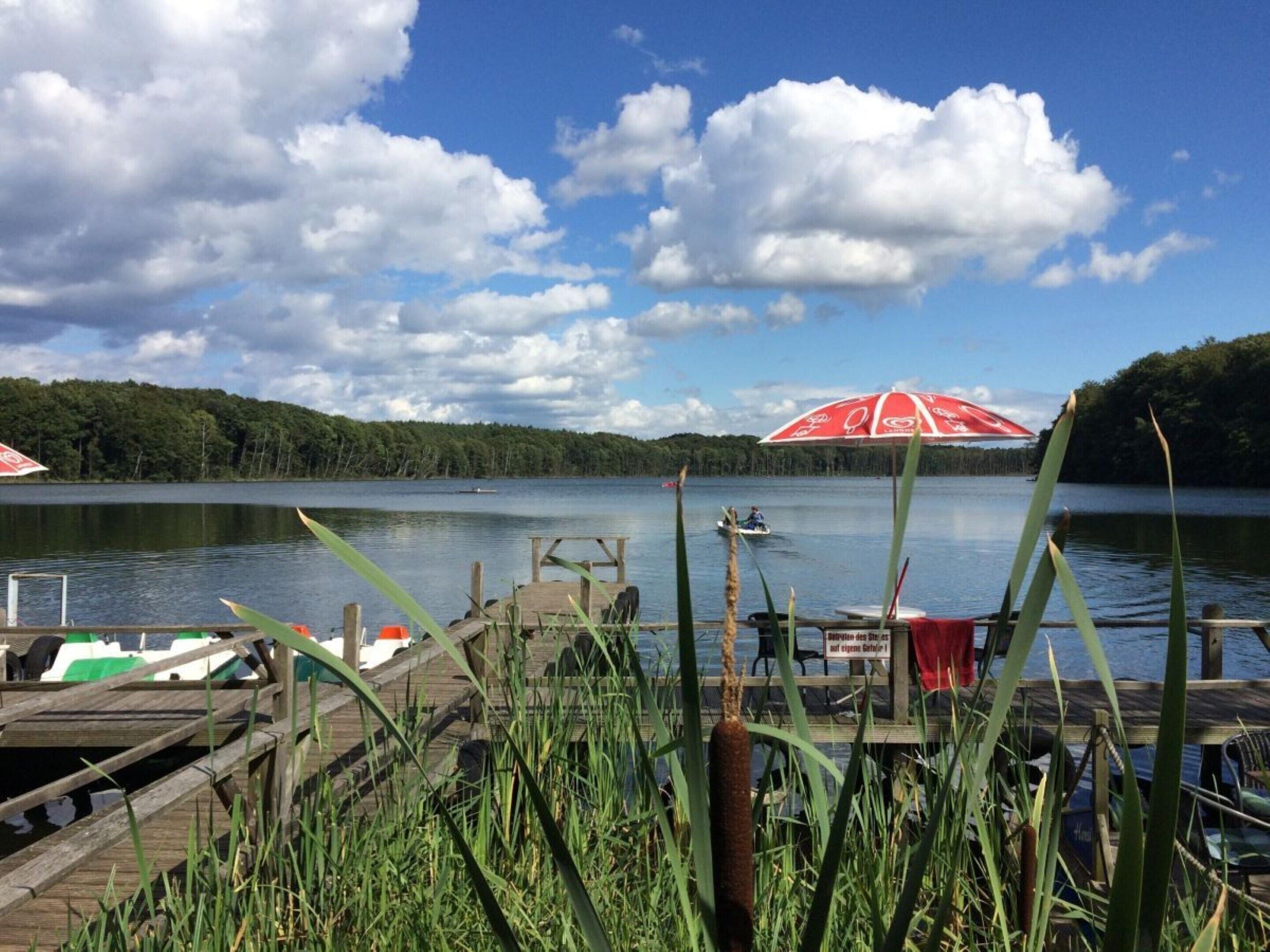 A lakeside dock with a boat, a red umbrella, and a wooden pier.