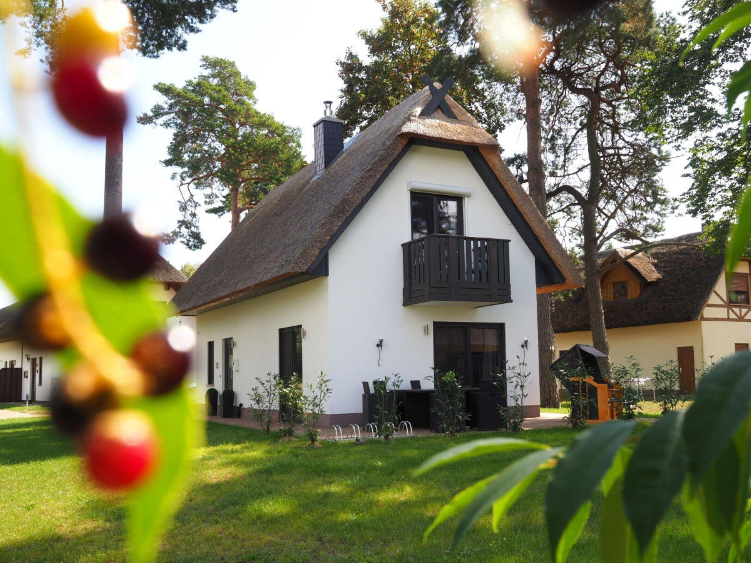A traditional house with a steep thatched roof, a balcony, and a well-maintained garden.