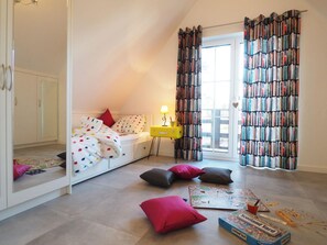 Ein Schlafzimmer mit einem Bett, einem Nachttisch, einer Lampe, einem Fenster mit Vorhängen und einem Bücherregal.