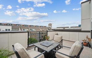 Ein Balkon mit Tisch und Stühlen, einem Blumentopf und Blick auf Gebäude im Hintergrund.