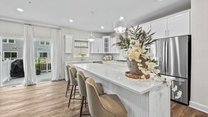 A modern kitchen with a central island, bar stools, stainless steel appliances, and a large window. - Luxury Furnished 3BR Townhome-Walk to Rio and Crown Plaza Garage-Modern Finishes (Gaithersburg)