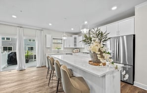 A modern kitchen with a central island, bar stools, stainless steel appliances, and a large window. - Luxury Furnished 3BR Townhome-Walk to Rio and Crown Plaza Garage-Modern Finishes (Gaithersburg)