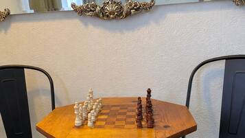 A chessboard set on a wooden table with two black chairs.
