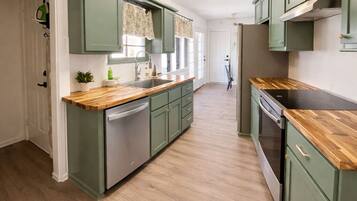 A kitchen with green cabinets, wooden countertops, and a dishwasher.
