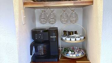 A kitchenette with a coffee maker, a microwave, and a shelf with cups and bowls.