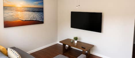 Een woonkamer met een bank, een flatscreen televisie, een plafondventilator en een schilderij van een zonsondergang boven de oceaan.