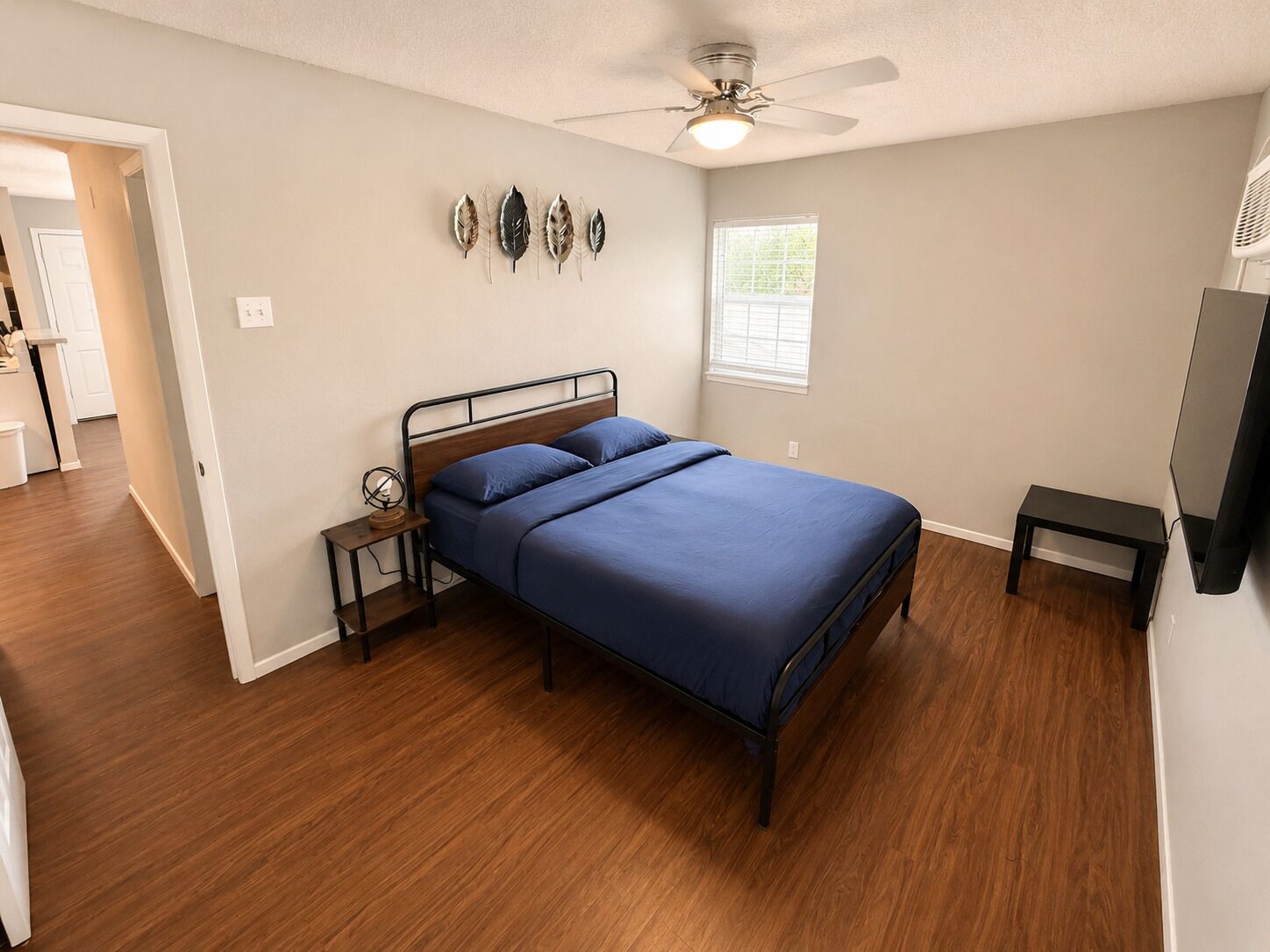 A bedroom with a bed, a nightstand, a ceiling fan, a window, and a television.