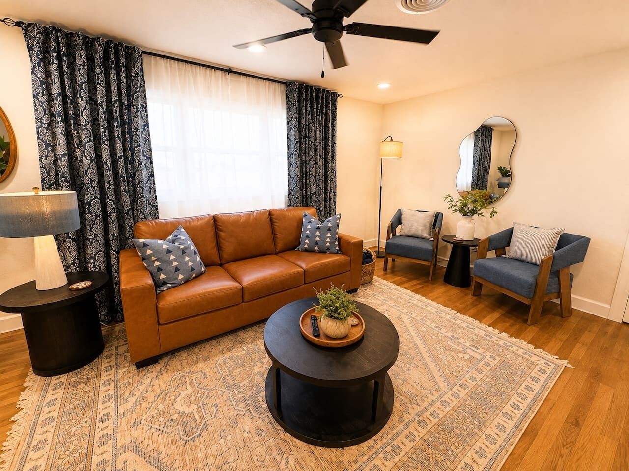 A living room with a brown leather sofa, a round coffee table with a plant, a blue armchair, and a floor lamp.