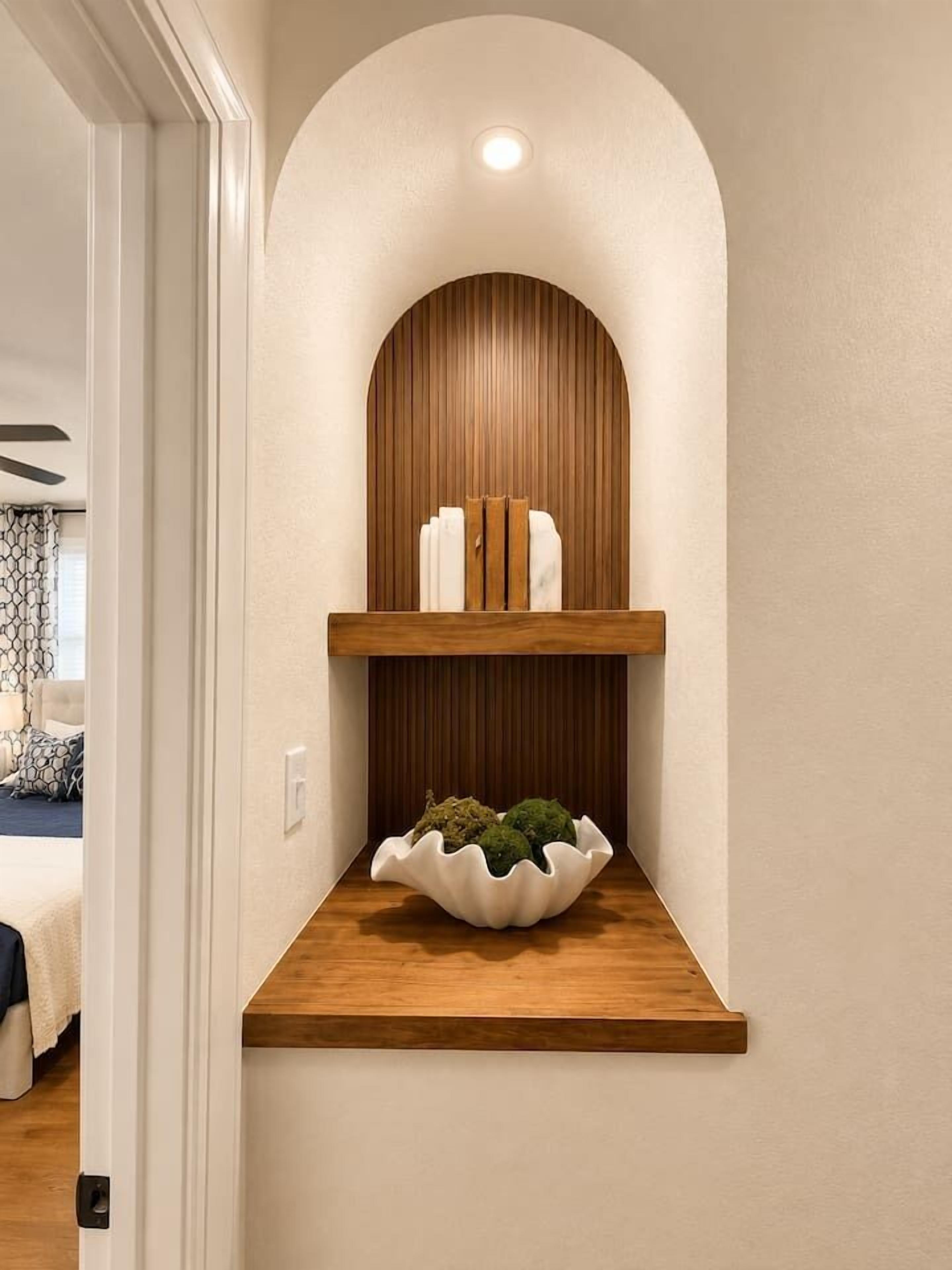 Um corredor com estante de madeira sob um nicho em arco, parede branca e porta que dá para outro cômodo.