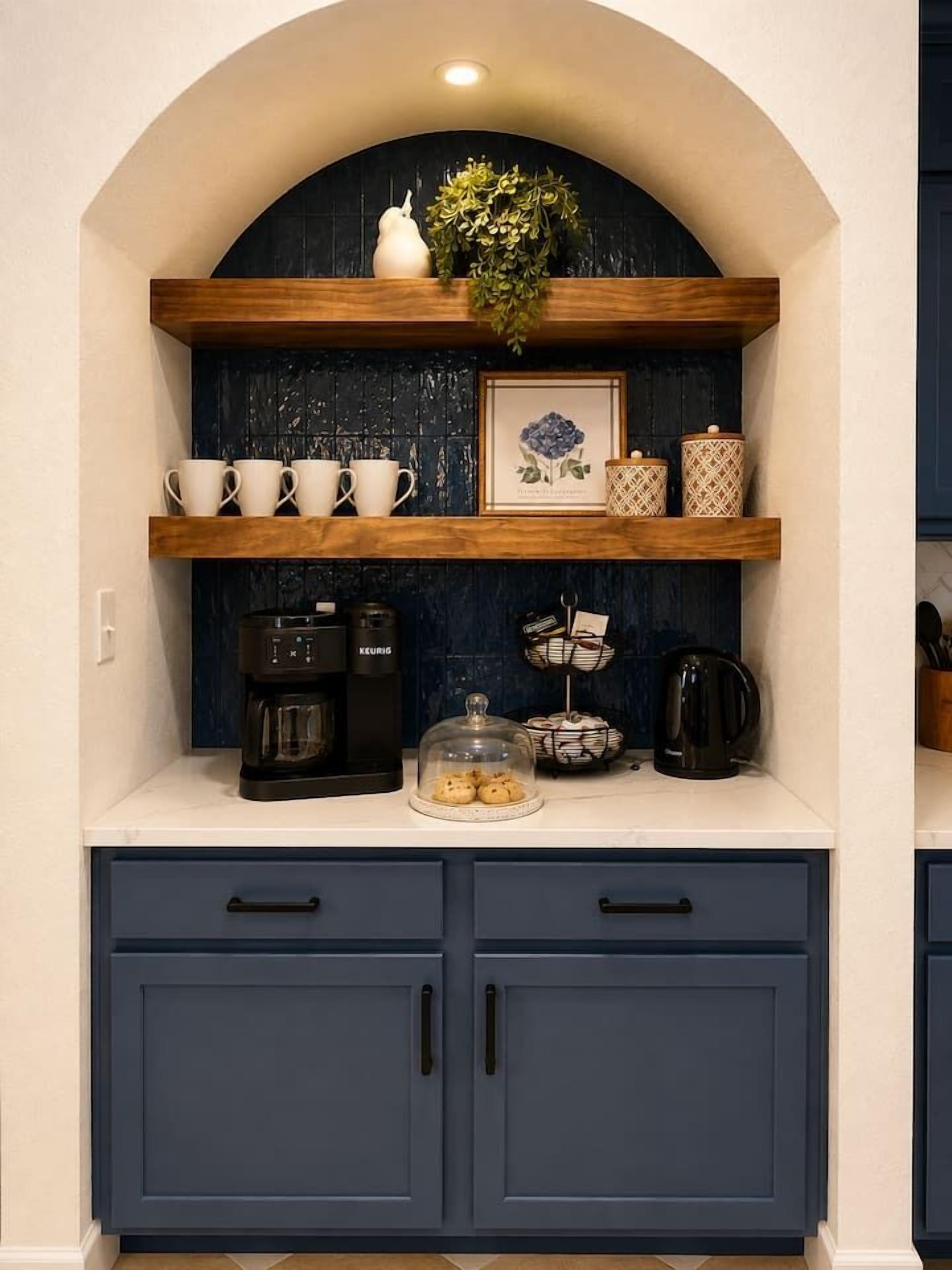 A kitchen with dark blue cabinets, a coffee maker, and a shelf with cups and a framed picture.