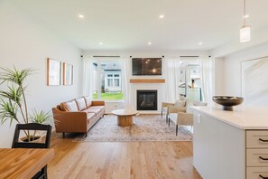 Una sala de estar moderna con chimenea, un sofá, una mesa de centro y un comedor con mesa de madera.
