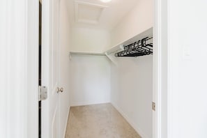 Un couloir étroit avec un placard contenant une étagère en métal et une porte dotée d’un loquet.