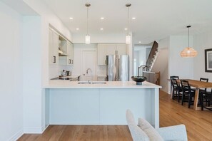 Une cuisine moderne dotée d’un îlot central, d’appareils électroménagers en acier inoxydable et de luminaires suspendus.