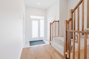 Un pasillo con una escalera de madera, un felpudo y una puerta que da a otra habitación.