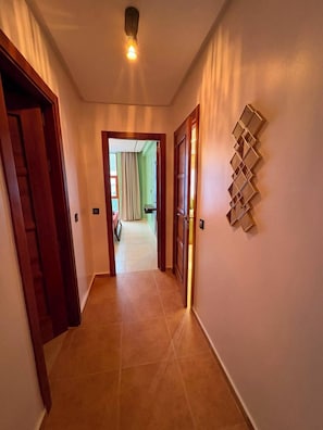 A hallway with wooden doors, a tiled floor, and a wall-mounted light fixture. - Comfortable Apartment / Downtown Tangier (Tanger)