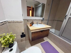 A bathroom with a white sink, a mirror above it, a wooden cabinet below, and a shower area to the right. - Comfortable Apartment / Downtown Tangier (Tanger)