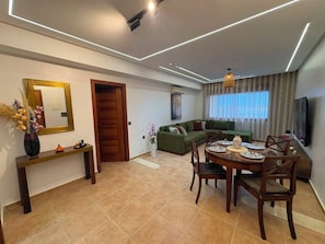 A modern living room with a dining area, a sofa, a TV, and a wooden door. - Comfortable Apartment / Downtown Tangier (Tanger)