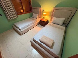 A room with two single beds, a nightstand with a lamp, a window with blinds, and a curtain. - Comfortable Apartment / Downtown Tangier (Tanger)
