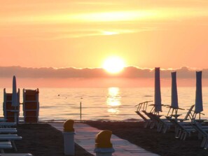 En strandscen med en solnedgång, strandstolar och parasoller.