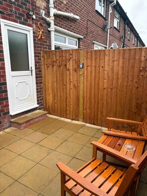 A wooden patio with a bench and a tiled floor, a white door, and a brick wall. - New apartment in prescot own access (Prescot)