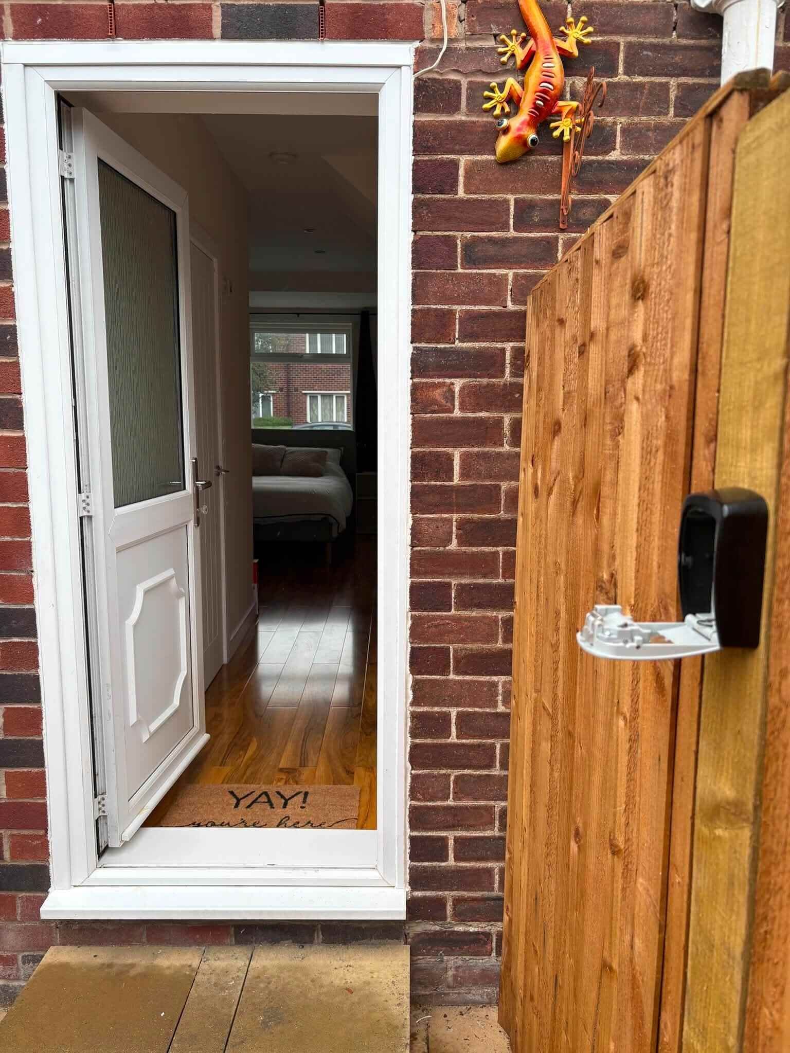 A doorway leading to a room with a bed and a window, a wooden fence, and a welcome mat with 'YAY!' on it.