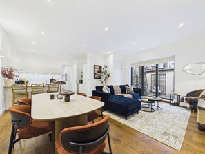 A modern living space with a dining area, a sofa, and a view through a large window. - Spacious Baker Street Apartment with Balcony (Greater London)