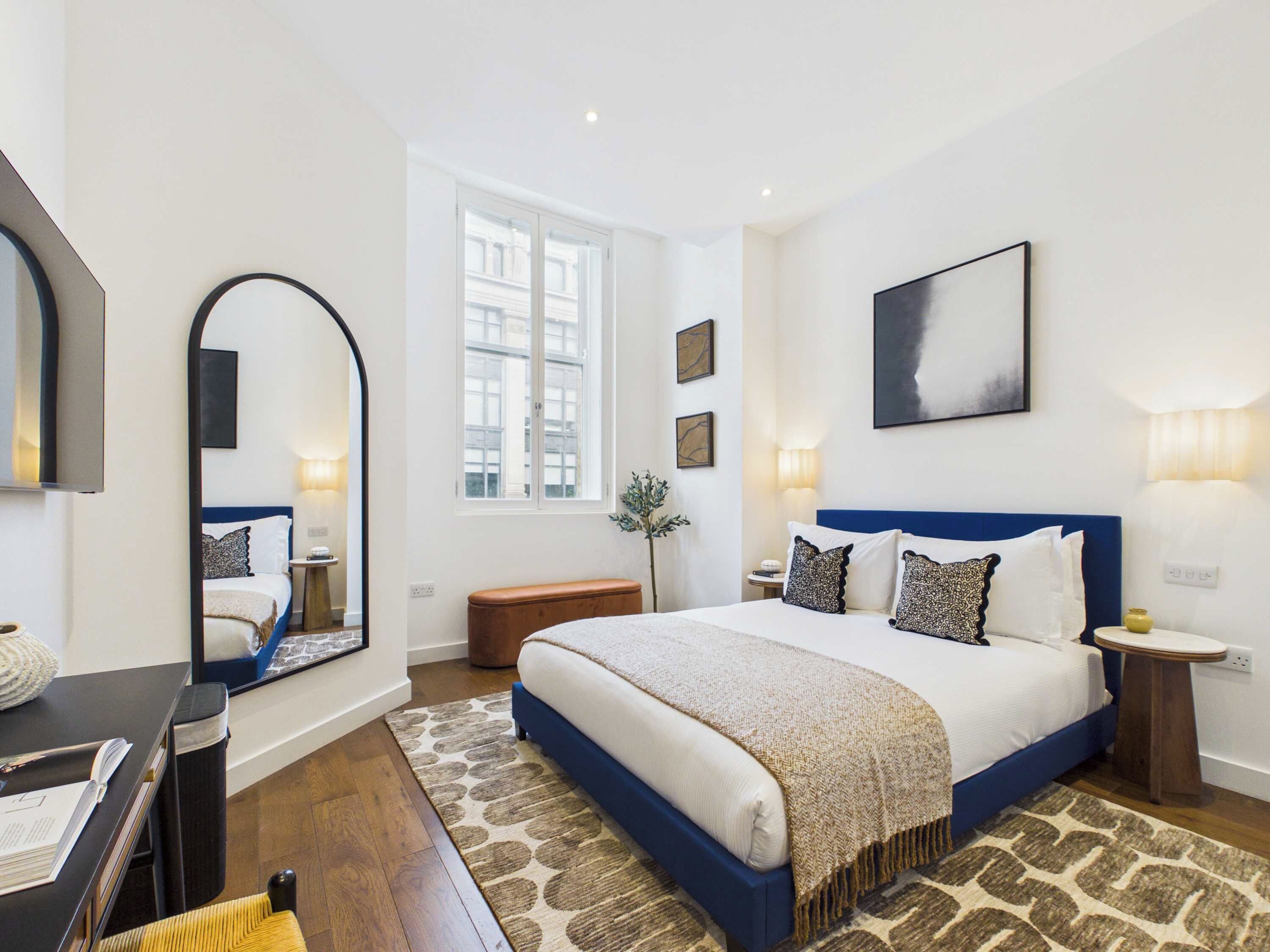 A modern bedroom with a large bed, a mirror, a window, and a painting on the wall.
