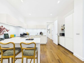 A modern kitchen with white cabinetry, a central island, and wooden chairs. - Spacious Baker Street Apartment with Balcony (Greater London)
